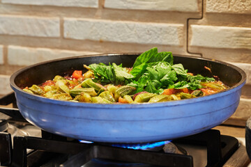 Okra and fried purple onions are pan-fried with cilantro and basil on gas stove