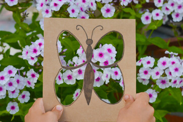 Development of children's fantasy and imagination. A butterfly cut out of a cardboard box against the background of pink phlox flowers, what to do with children in the summer.