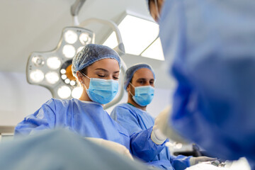 Group of surgeons at work in operating theater toned in blue. Medical team performing operation