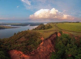 a high bank of clay with fields and trees, clouds in the sunset light, the sun and the riverbed of the Ob