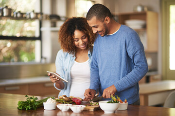 Digitizing their diet plan. Shot of a happy young couple using a digital tablet while preparing a...