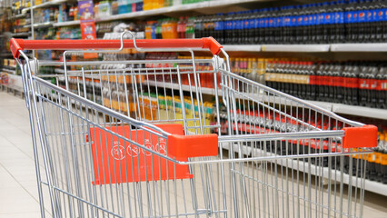 Close-up of a shopping trolley against many shelves of different drinks in a supermarket