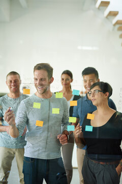 Confident manager, leader or boss talking in a meeting, workshop or presentation with sticky notes in the boardroom. Businessman talking, discussing and brainstorming with a group of colleagues