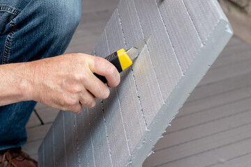 A worker cuts a sheet of extruded polystyrene with a clerical knife