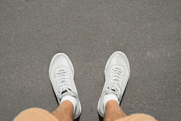Close-up of man in shorts wearing white summer sneakers with breathable ventilating mesh standing...