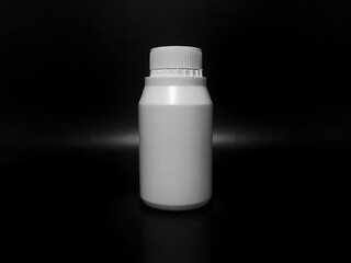 The empty plastic white bottle is on a dark background.