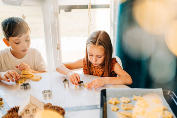 Happy kids cooking cookies bakery together and having fun with flour indoors at cozy home on the kitchen table. Siblings in big loving family