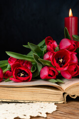 Book, tulips red candle and knitted napkin on dark wooden table Close-up