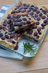 Sliced Italian Focaccia bread with sweet black grape and rosemary on a wooden table. Traditional dessert from Tuscany in Italy called “schiacciata con l'uva”