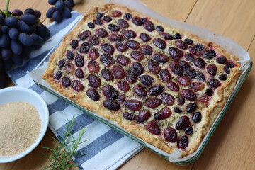 Italian Focaccia bread with sweet black grape and rosemary on a wooden table. Traditional dessert from Tuscany in Italy called “schiacciata con l'uva”