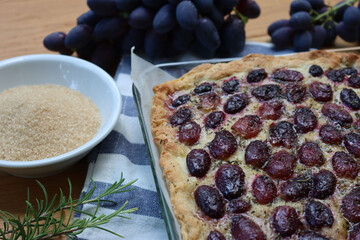 Italian Focaccia bread with sweet black grape and rosemary on a wooden table. Traditional dessert...