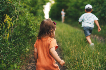 Rear view of a family of three climbing a green hill to reach home in the village, returning from the fields. Family exploring nature together. Happy family