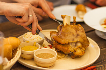 Married man's hands cuts a roasted pork knuckle with a knife and fork. Czech national cuisine.