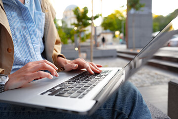 Close up of female hands typing on computer keyboard of a laptop sitting in the street