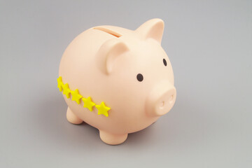 Piggy bank with 5 yellow rating stars on gray background close-up.