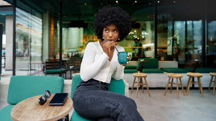 Young afro woman taking break and drinking coffee in cafe