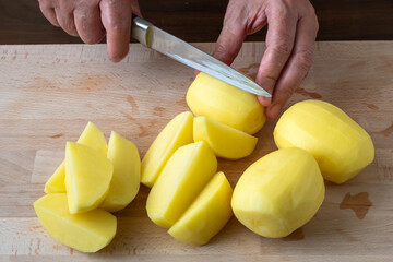 Hands with knife cutting potatoes, preparing potatoes for cooking.