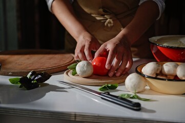 Details: Chef's hands holding ripe juicy red tomatoes and mushroom champignon. Fresh organic vegetables on kitchen table