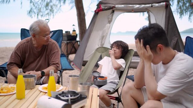 Asian family with senior and kids relaxing and camping on tropical beach during summer holiday. Togetherness and outdoor activity lifestyle.