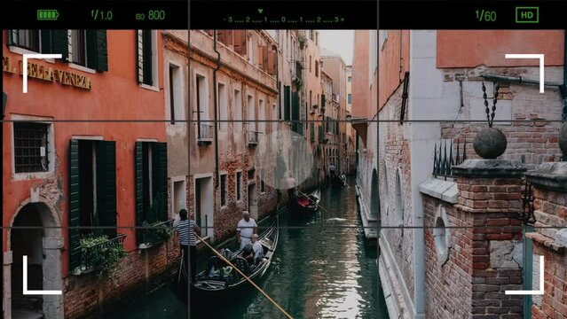 Venice, Italy - July 2, 2022: A look through the photo camera at Venice narrow canal with historical buildings and gondolas, singer sings in a gondola