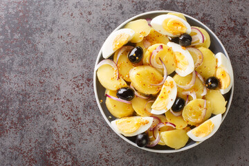 Oriental Romanian potato salad with boiled eggs, onion and olives seasoned with mustard sauce close-up in a plate on the table. horizontal top view from above