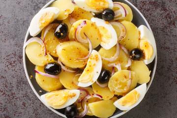 Potato salad with boiled eggs, onions and olives seasoned with mustard sauce close-up in a plate on the table. horizontal top view from above