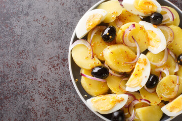 Romanian oriental potato salad with onions, olives and boiled eggs close-up on a plate on the table. horizontal top view from above