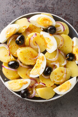 Oriental salad is a favorite of Romanians potato salad with onions, olives and boiled eggs close-up on a plate on the table. Vertical top view from above
