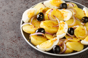 Potato salad with boiled eggs, onions and olives seasoned with mustard sauce close-up in a plate on the table. horizontal