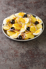 Salata orientala potato salad with onions, olives and boiled eggs close-up on a plate on the table. Vertical
