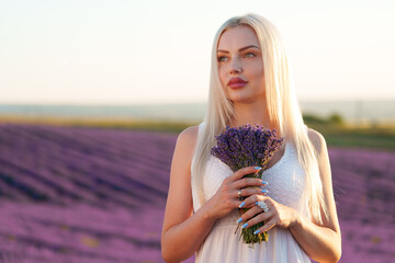 Portrait o charming blonde girl smells lavender flowers in lavender field