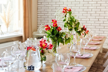 Glasses, forks, knives, napkins and a decorative flower on a dark brown wooden table served for dinner in a cozy restaurant