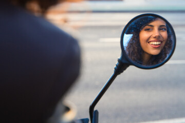 Young and beautiful woman with dark and curly hair is sightseeing in Seville. She is reflected in the rear-view mirror of an electric motorbike to move around the city. Renewable energy and tourism.