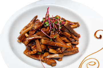 Fried pieces of pork in sauce decorated with microgreens. Marinated pig ears
