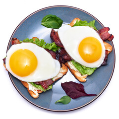 Fried eggs, bacon and cream cheese sandwiches on a plate on wooden table at domestic kitchen