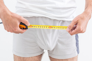 Young man holding tape measure, measuring his penis - focused at the middle of tape measure. - Powered by Adobe