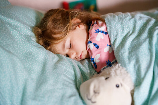 Cute little preschool girl sleeping in bed. Tired preschool child dreaming, healthy sleep of children. Hugging with soft toy.