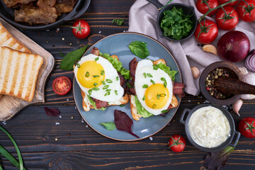 Fried eggs, bacon and cream cheese sandwiches on a plate on wooden table at domestic kitchen