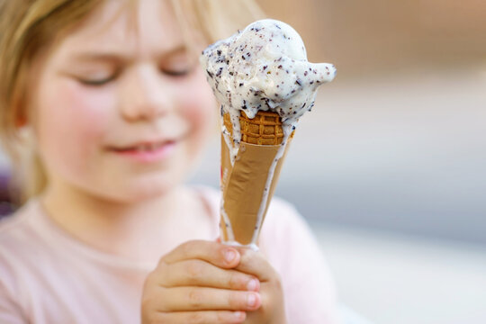Little preschool girl eating ice cream in waffle cone on sunny summer day. Happy toddler child eat icecream dessert. Sweet food on hot warm summertime days. Bright light, colorful ice-cream