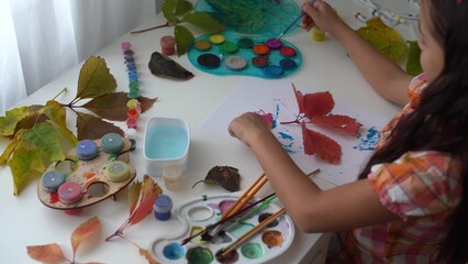 Little girl painting on autumn yellow leaves with gouache, kids arts, children creativity, autumn art.