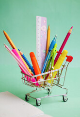 in a cart from a hypermarket there are many different school supplies on the background of a blackboard at school and chalk