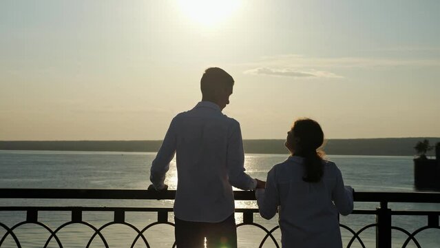 Young couple looks together at river. Man and woman with cerebral palsy enjoy spending time together on embankment at back sunset light