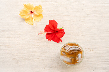 Top view iced coffee next to hibiscus flowers on the beach.