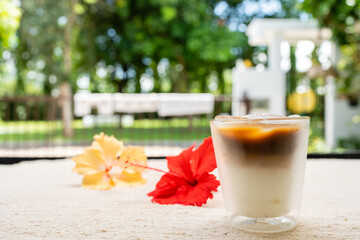 Iced coffee with milk next to hibiscus against nature background.