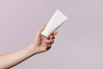 Hand holds blank white plastic tube on pink background. Cosmetic beauty product branding mock-up....