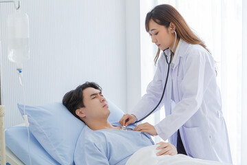 Fototapeta premium Female doctor and young male patient who lie on the bed while checking pulse in hospital wards.