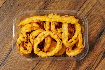Onion rings serving in a plastic tray on wooden table surface background. Simple food with high calorie and fat count. Beer snack.