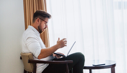 Male businessman in a white shirt working at a laptop in the office, during a conversation, online meeting, remote work.