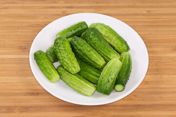 Whole small cucumbers on a dish on a wooden surface