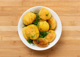 White plate with fried potatoes sprinkled with dill on a wooden table, top view